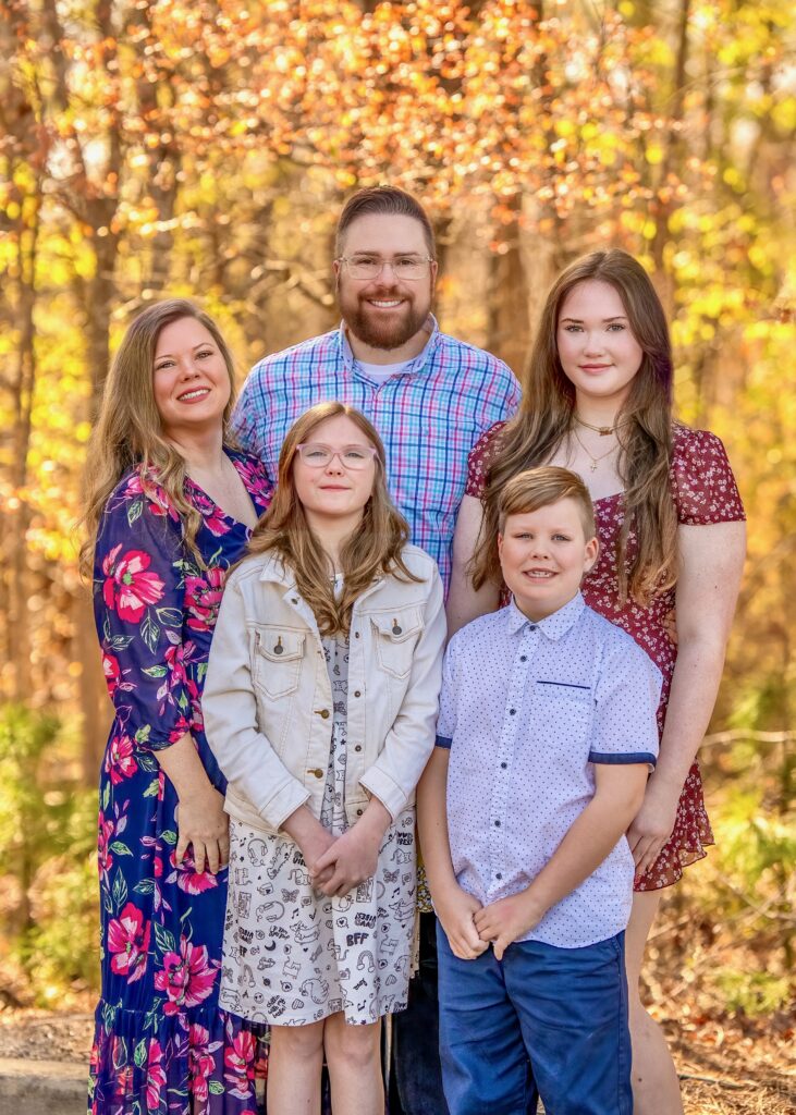 Family of five standing together outdoors among golden autumn trees.